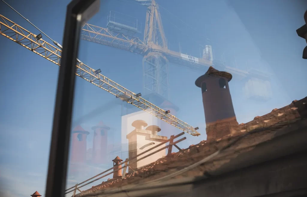 Gru di cantiere riflesse su una vetrata sopra i tetti.