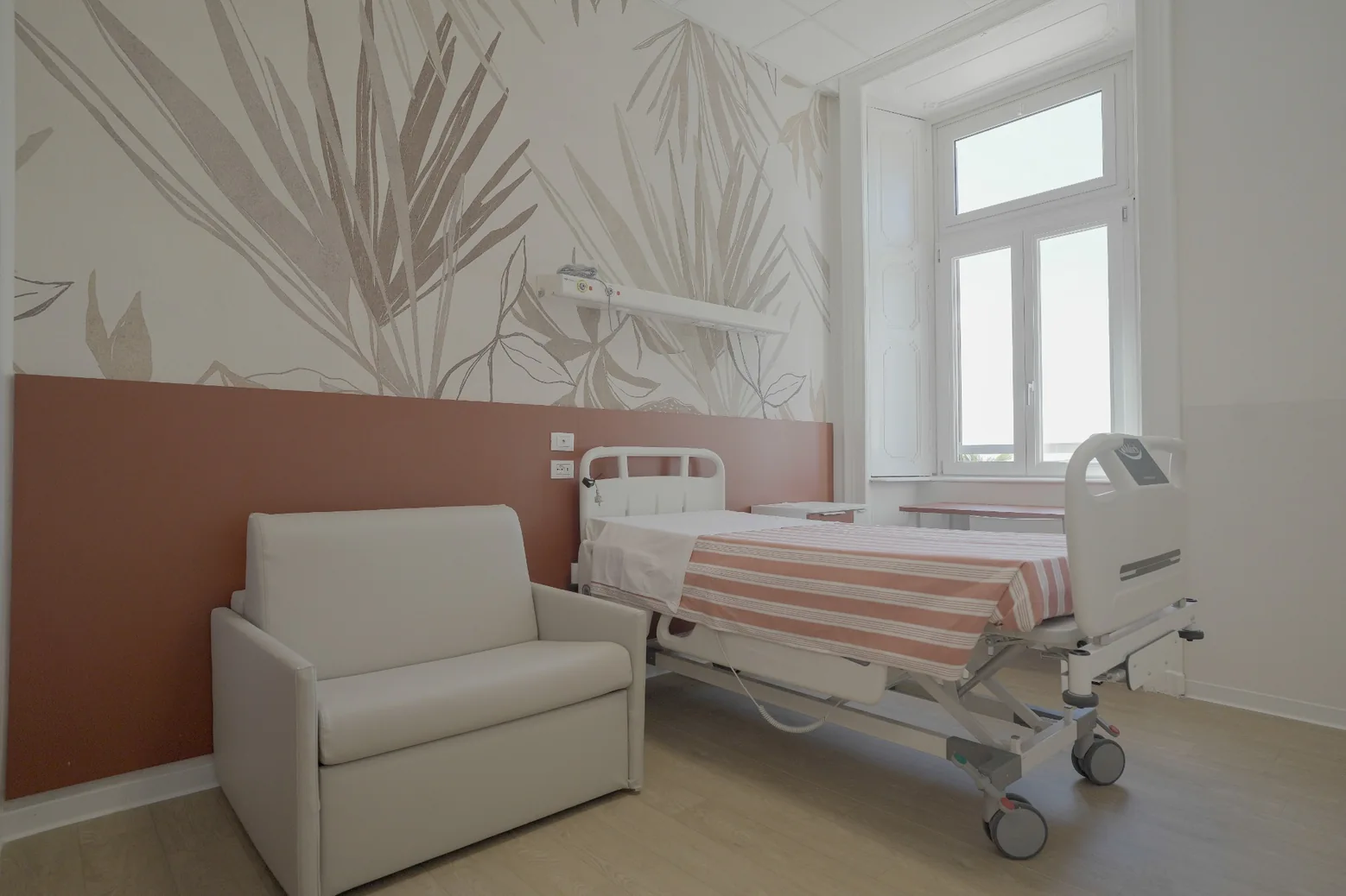 Camera di degenza con letto, poltrona letto e parete decorata nei toni terracotta.